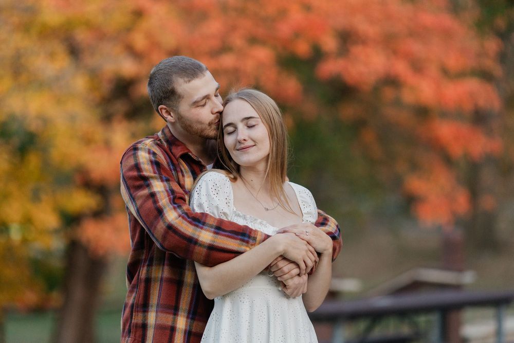 A romantic couple embraces in front of vibrant autumn foliage during a fall photo session.