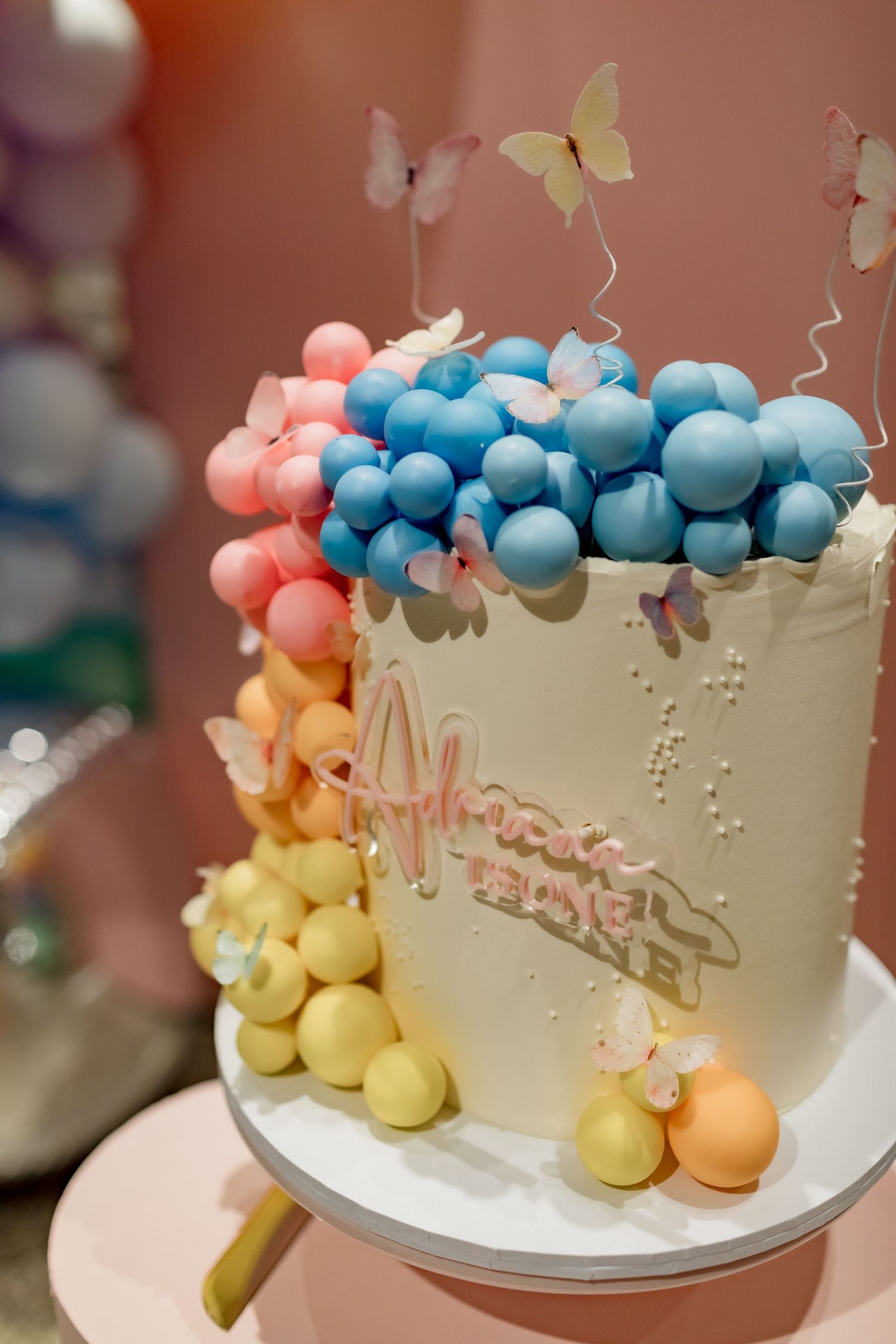 Elegant white birthday cake adorned with colorful balloon designs and delicate butterfly decorations.
