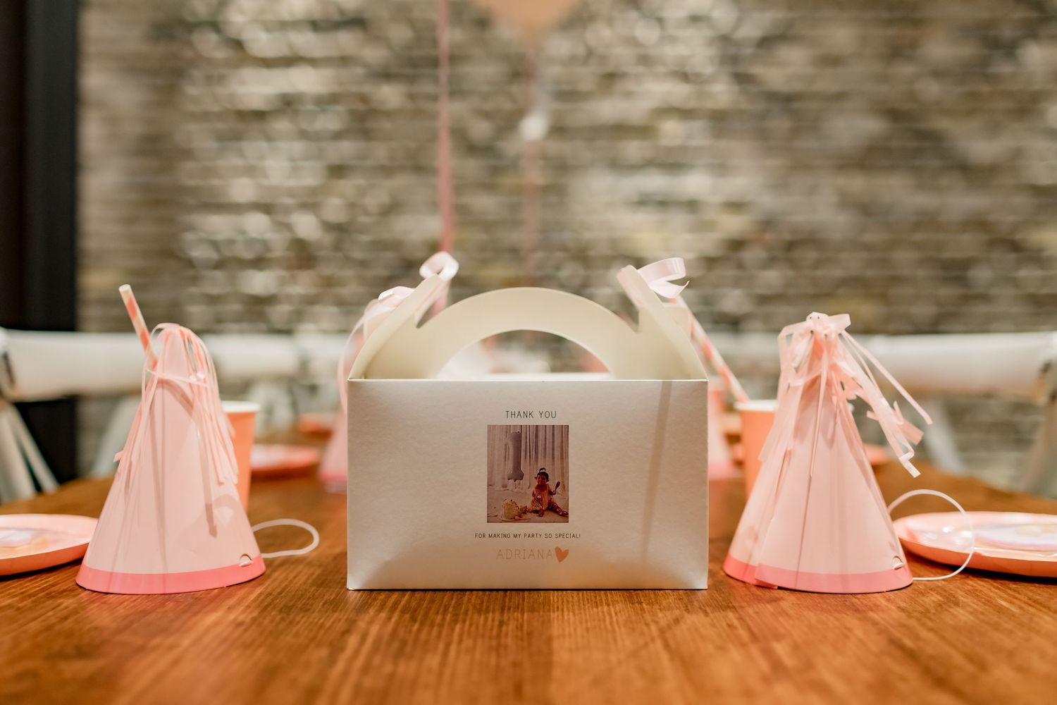 Pink party favor boxes and party hats arranged on wooden table for celebration.