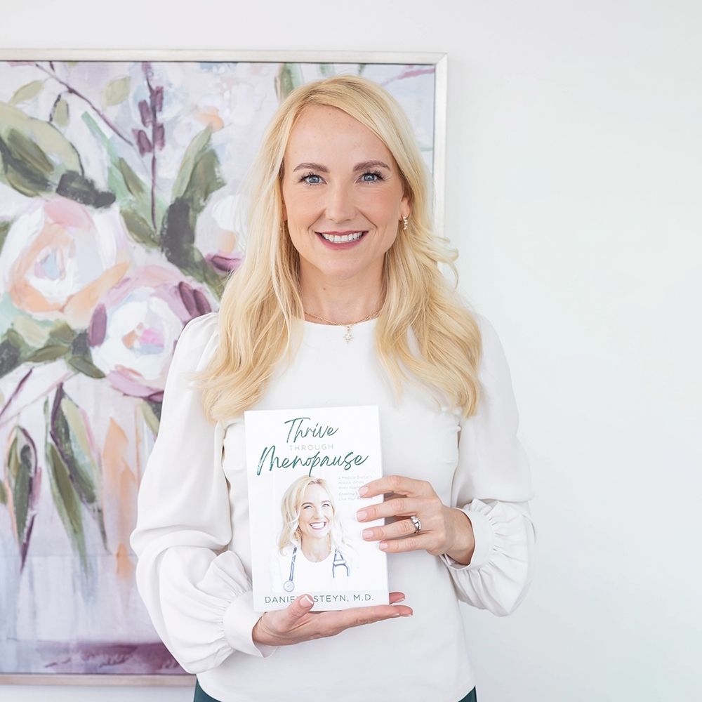 Woman in white sweater holds book with floral artwork in background.
