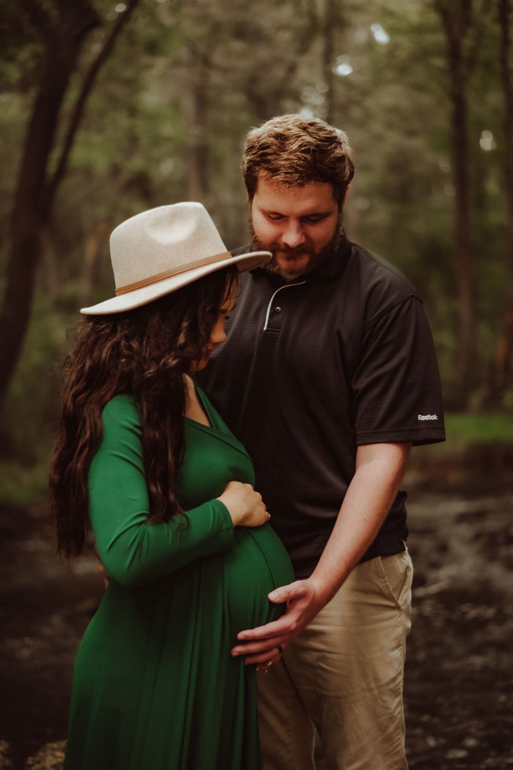 Couple shares tender moment in forest setting with woman in emerald dress.
