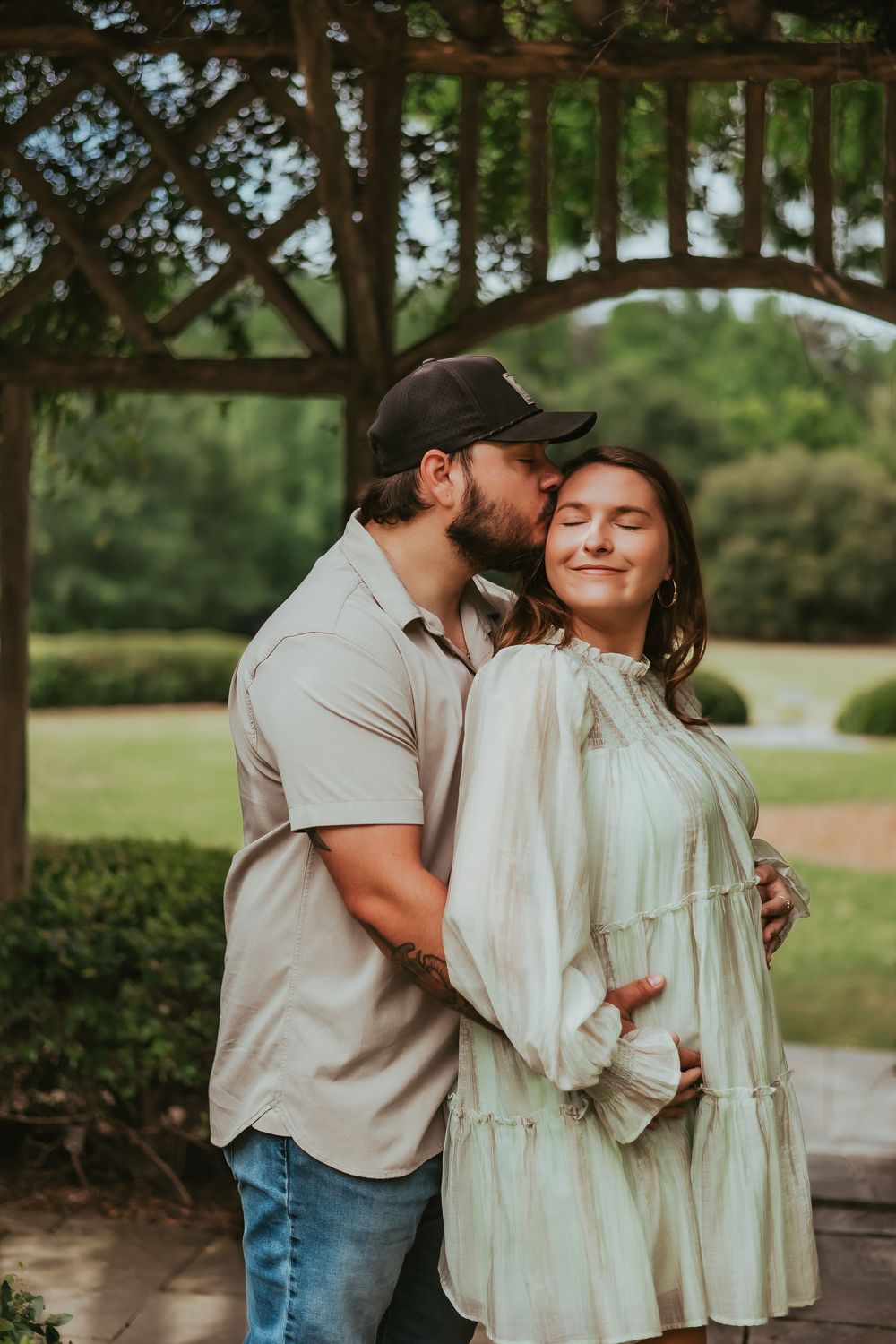 A couple sharing tender moments under a wooden pergola in a garden setting.