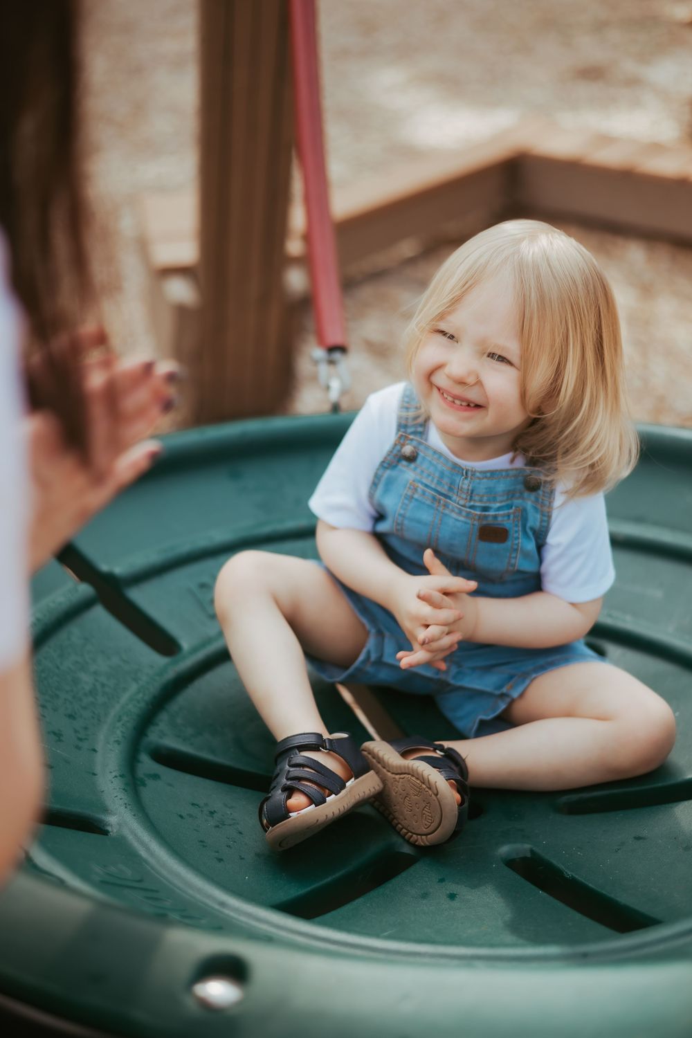 A small child playing and smiling while sitting on a green merry-go-round.