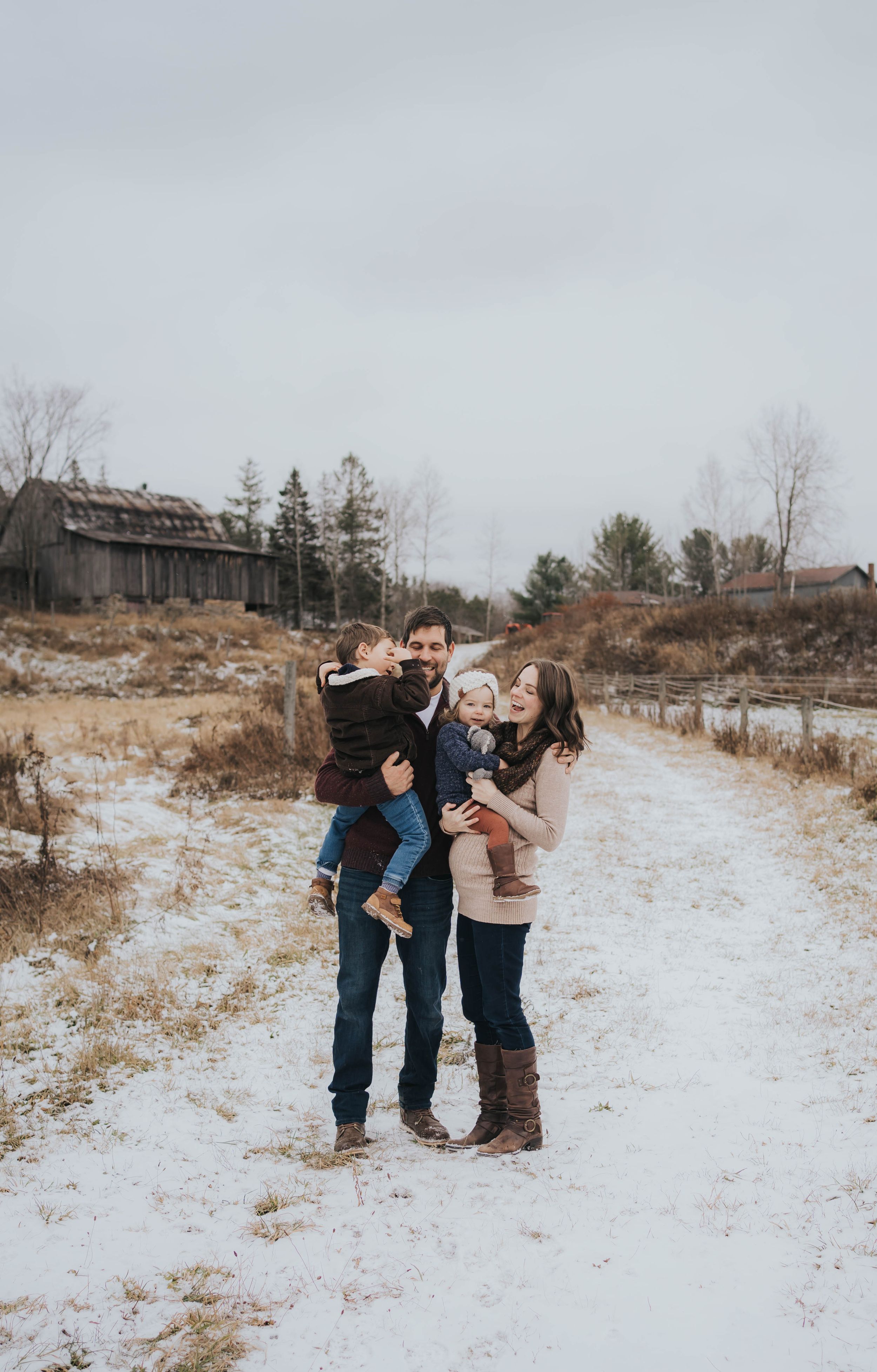 A family shares joyful moments together on a snow-covered path with rustic buildings in background.