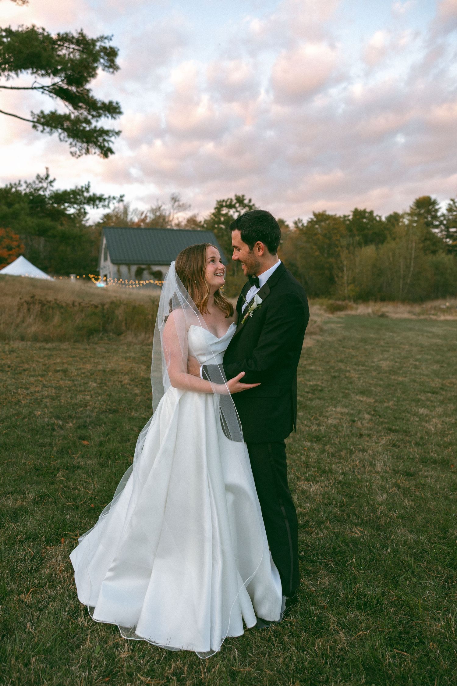 Romantic sunset wedding portraits in an open field with white tent in background.