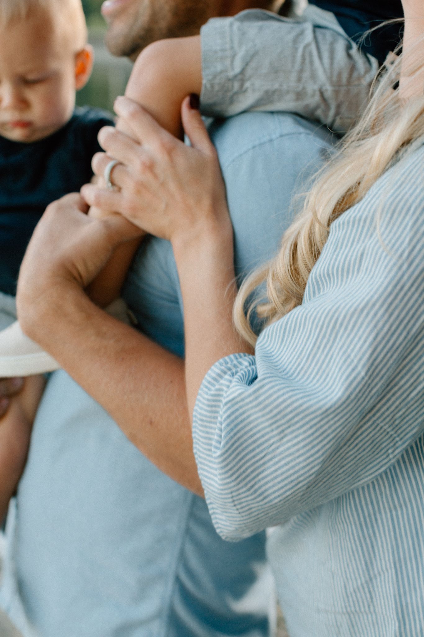 Close-up of a woman in a striped top embracing a man holding a baby.