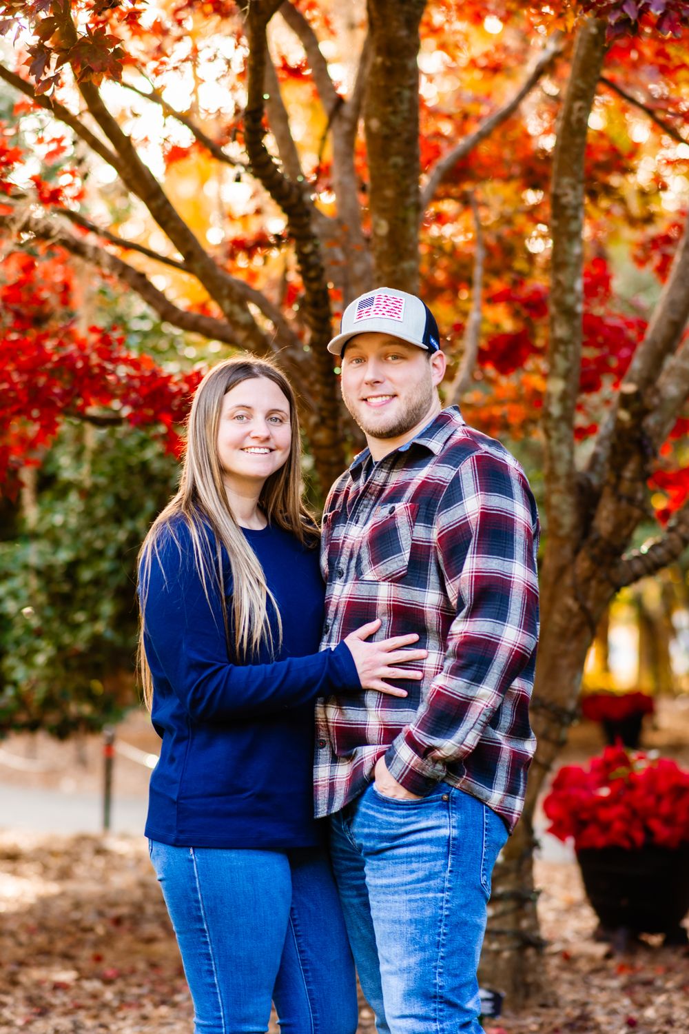 A couple poses outdoors together surrounded by vibrant red autumn foliage and fall colors.