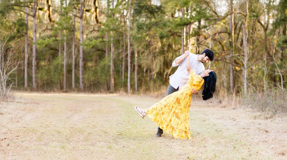 Couple dances together in nature setting, with woman in flowing yellow dress and tall pine trees in background.