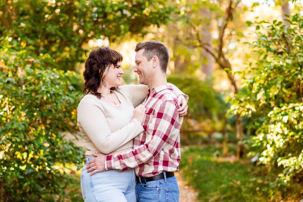 A couple embraces in a romantic outdoor photoshoot surrounded by lush greenery and golden sunlight.