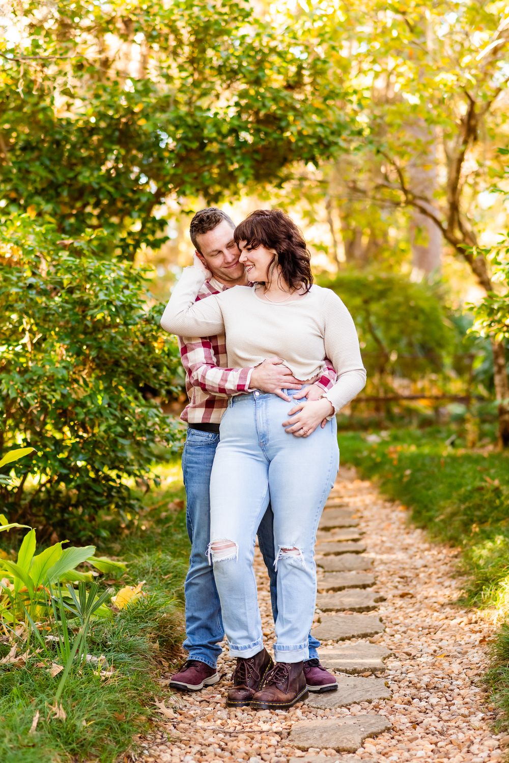 A couple shares tender moments on a leaf-covered autumn path in a wooded area during a fall photoshoot.
