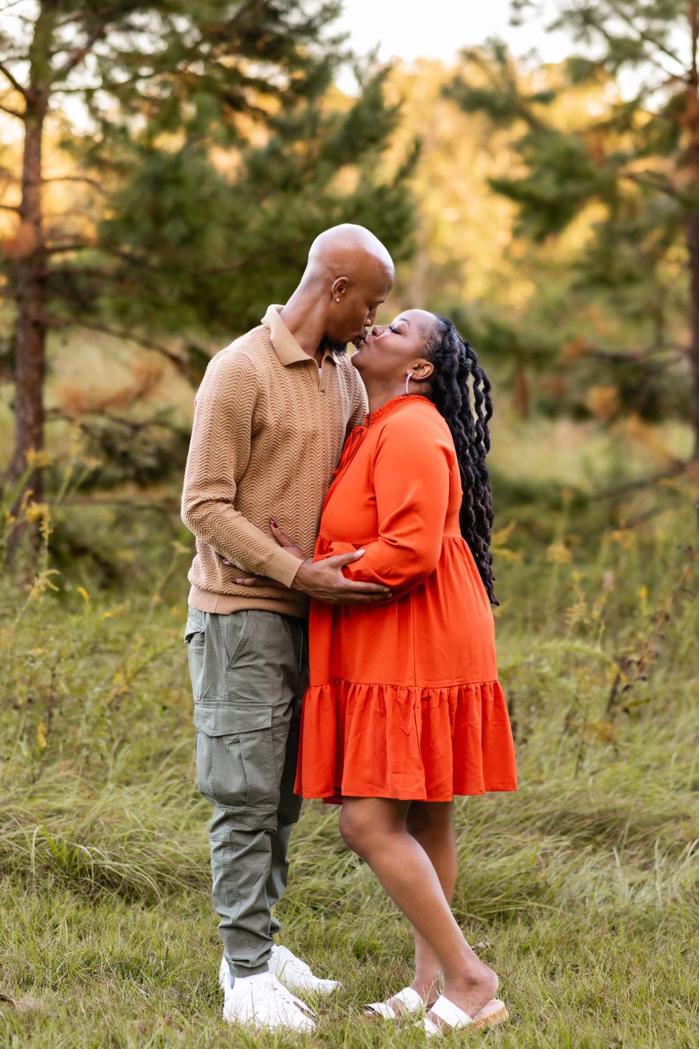 A couple sharing an intimate moment outdoors during autumn, with pine trees and golden foliage in the background.