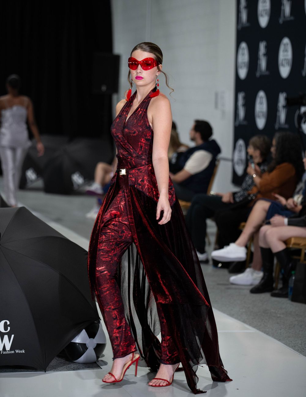 Runway model in red velvet jumpsuit with matching mask and flowing black overlay.