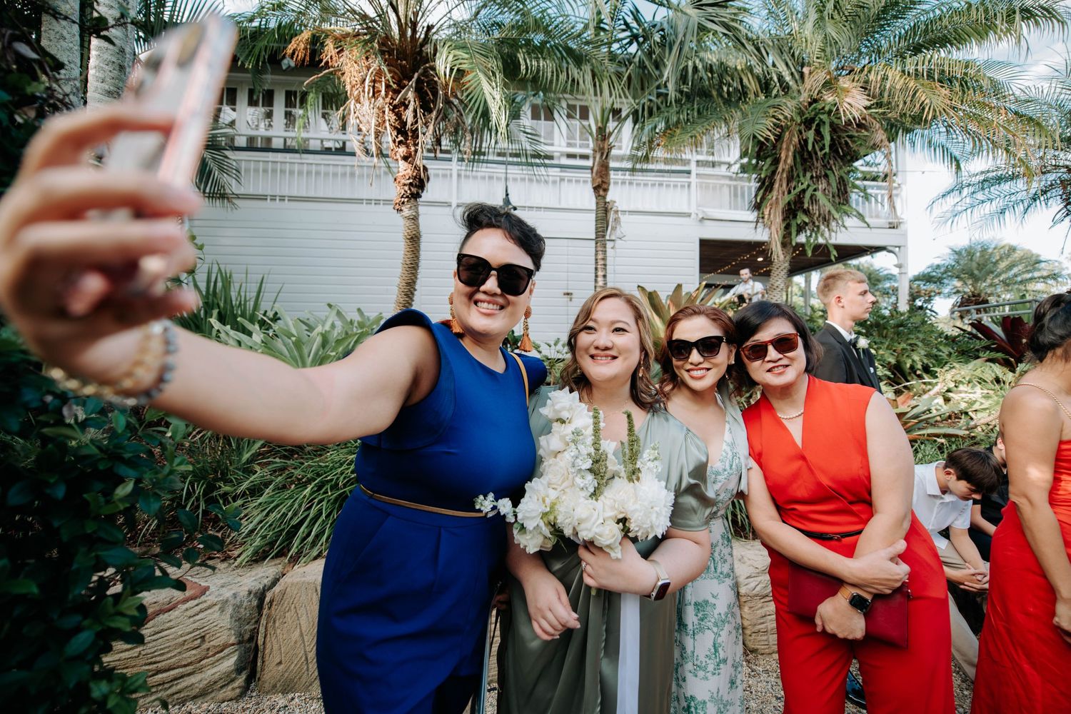 Wedding party taking a group selfie outdoors with palm trees in the background.