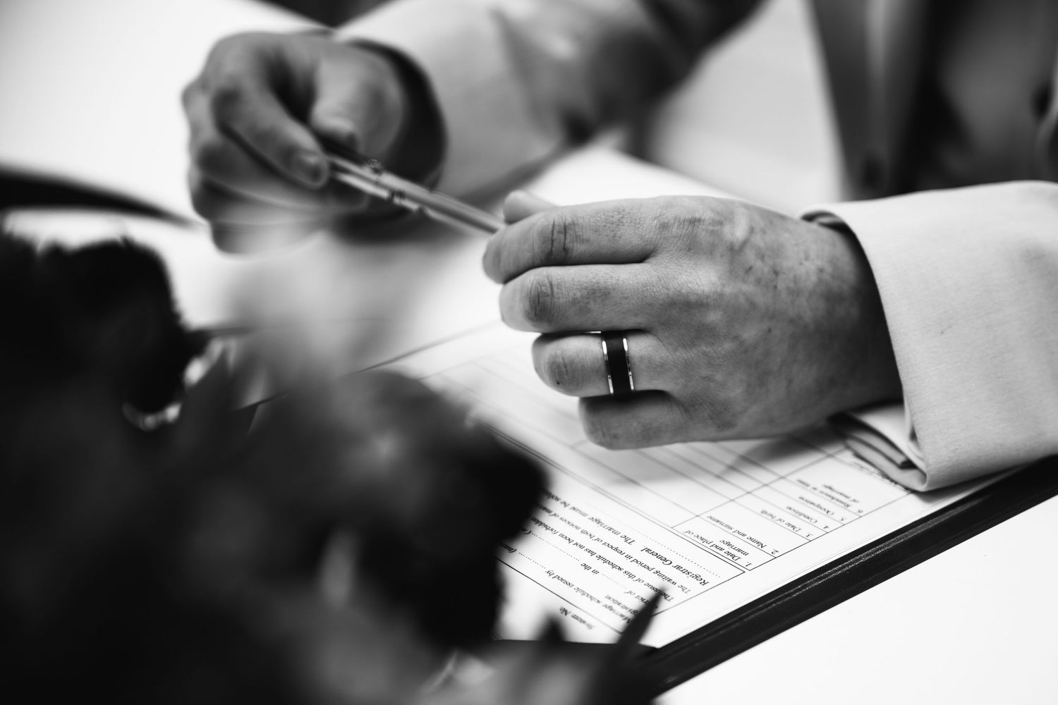 Black and white close-up shots of hands signing wedding documents.