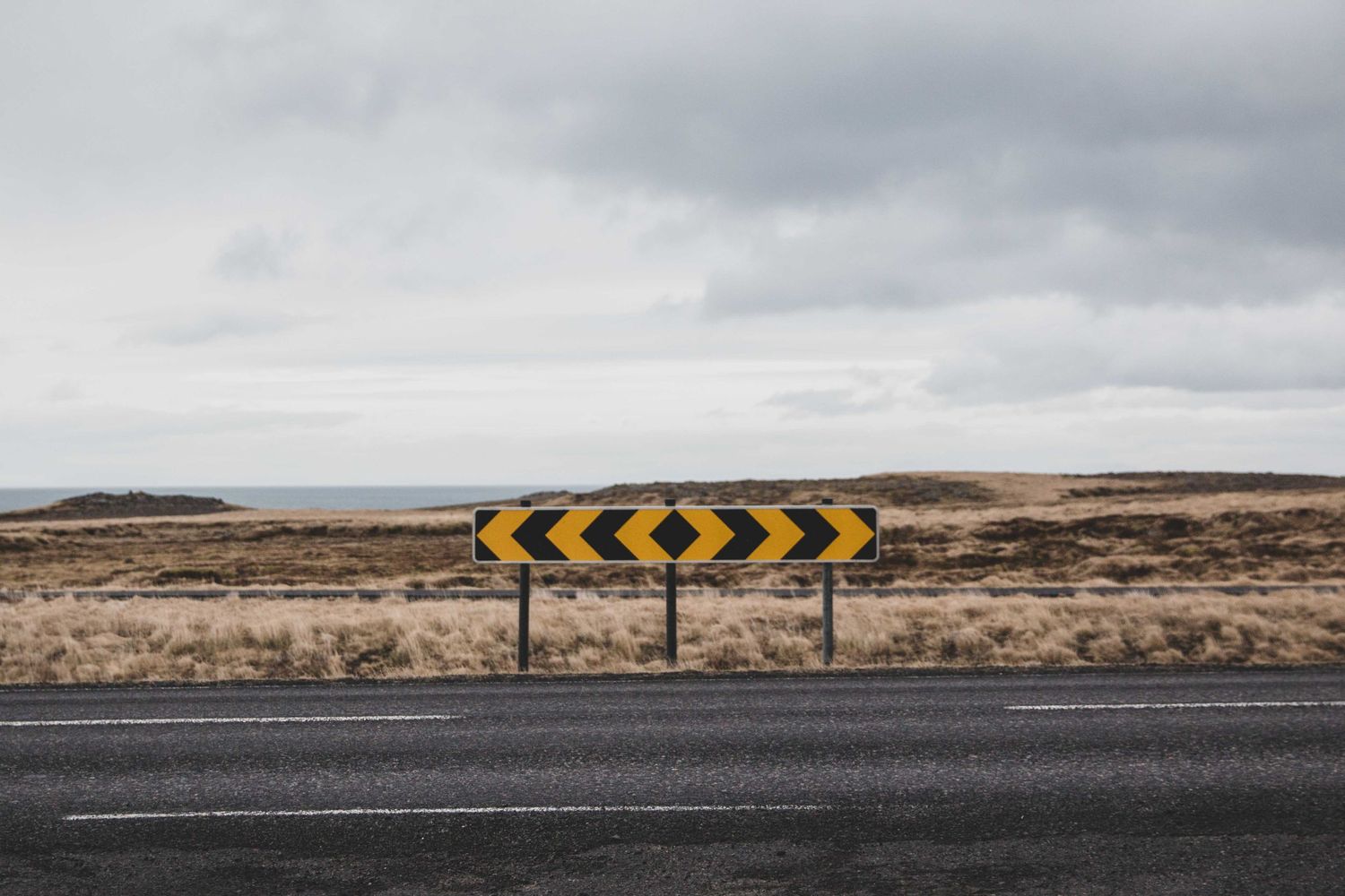 Yellow chevron warning signs on rural road with barren landscape.