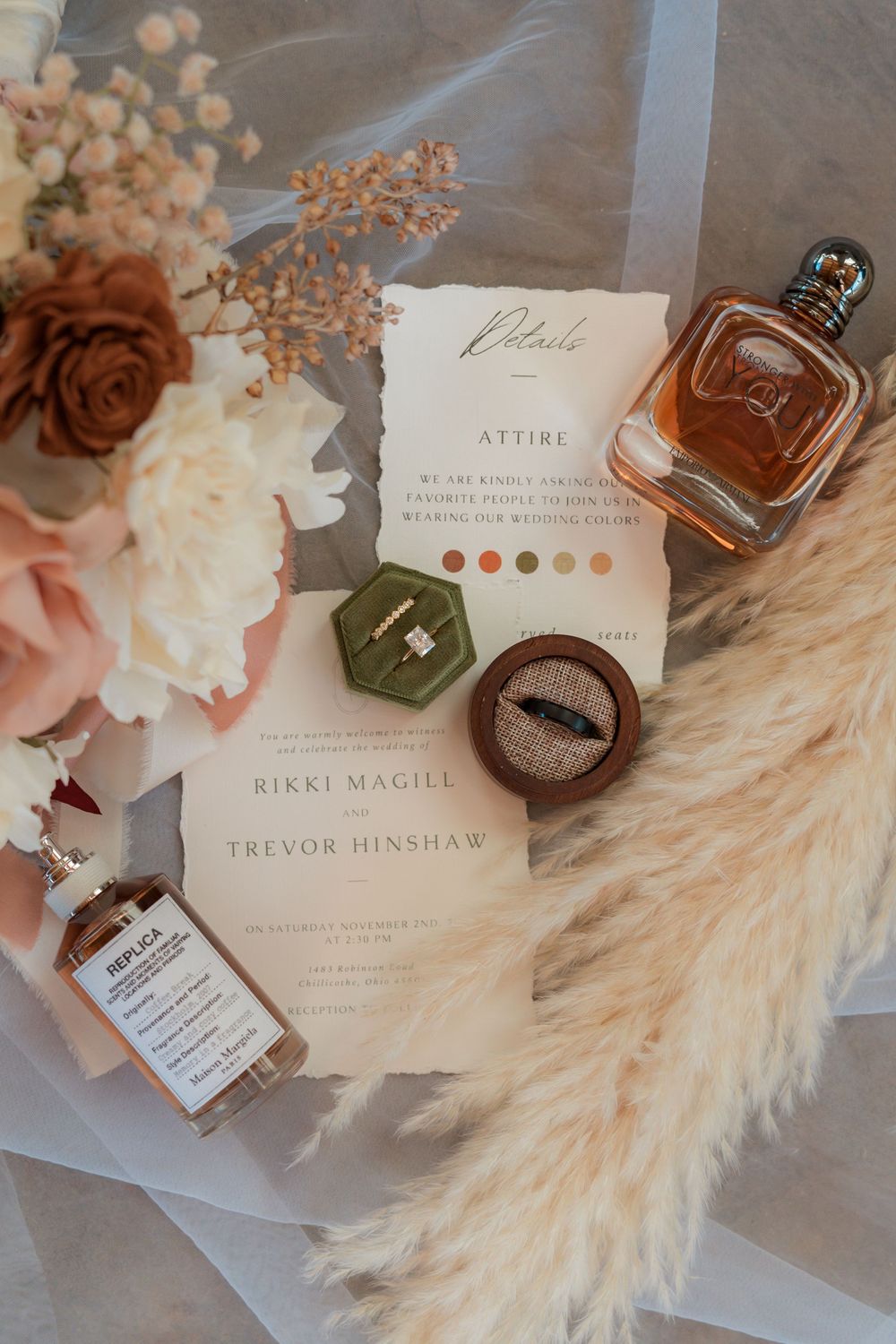 Wedding details flatlay with invitation, perfume bottle, and dried flowers on textured surface.