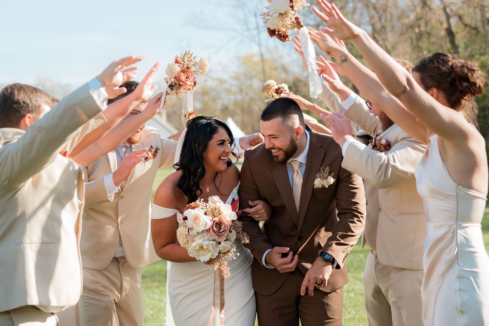A wedding party walks through a sunlit garden in coordinated neutral attire.