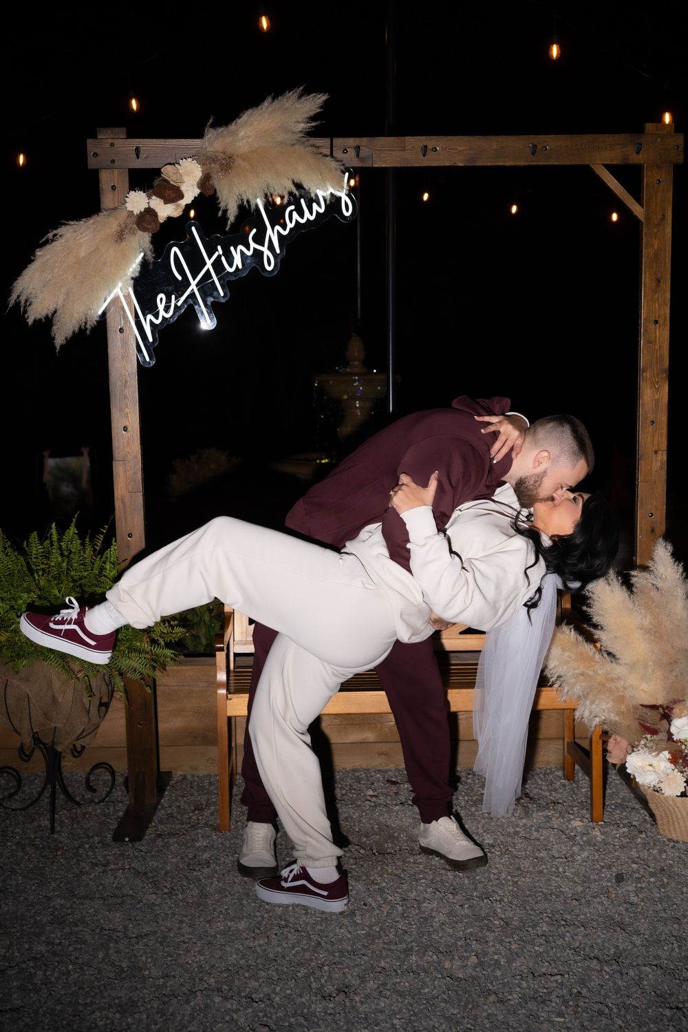 Romantic dip pose under a decorated wooden arch with white feather decorations at night.