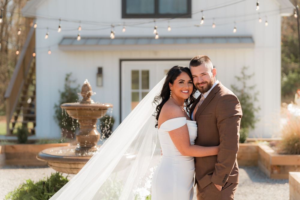 A romantic wedding portrait of a couple embracing in front of a white building with a decorative fountain.