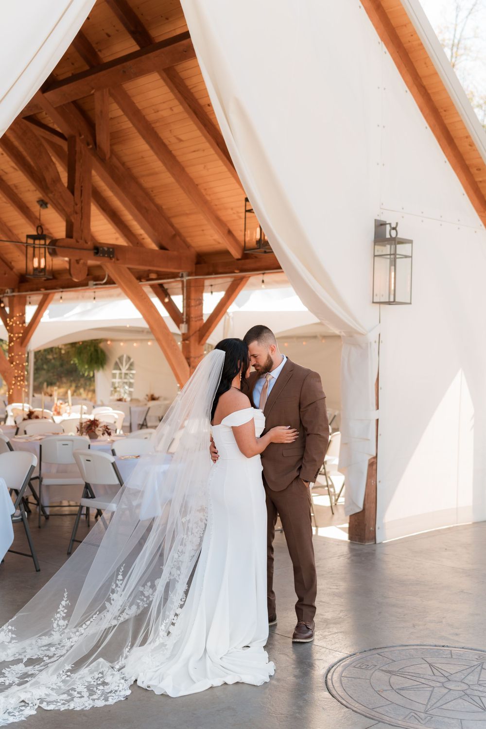 A wedding couple shares an intimate moment under a rustic timber beam pavilion.
