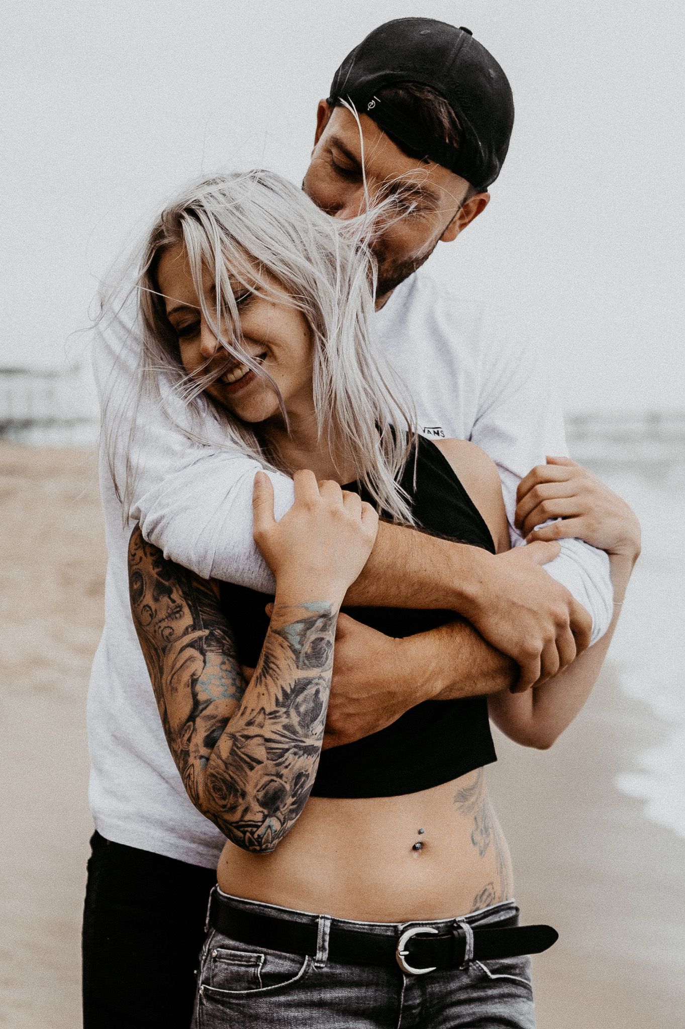 Intimate beach portrait of couple embracing with ocean waves in background.