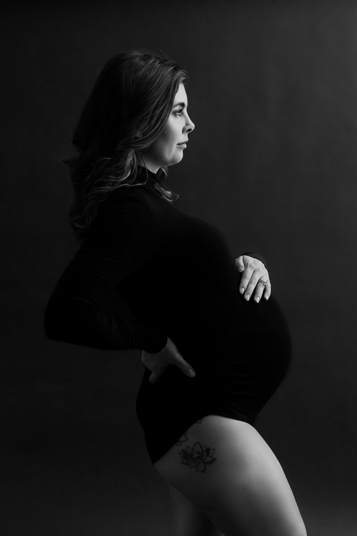 Artistic black and white maternity portrait showing silhouette against dark background.