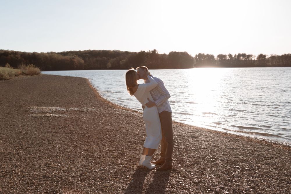 Couple embraces in a romantic moment at sunset on a rocky beach shoreline.