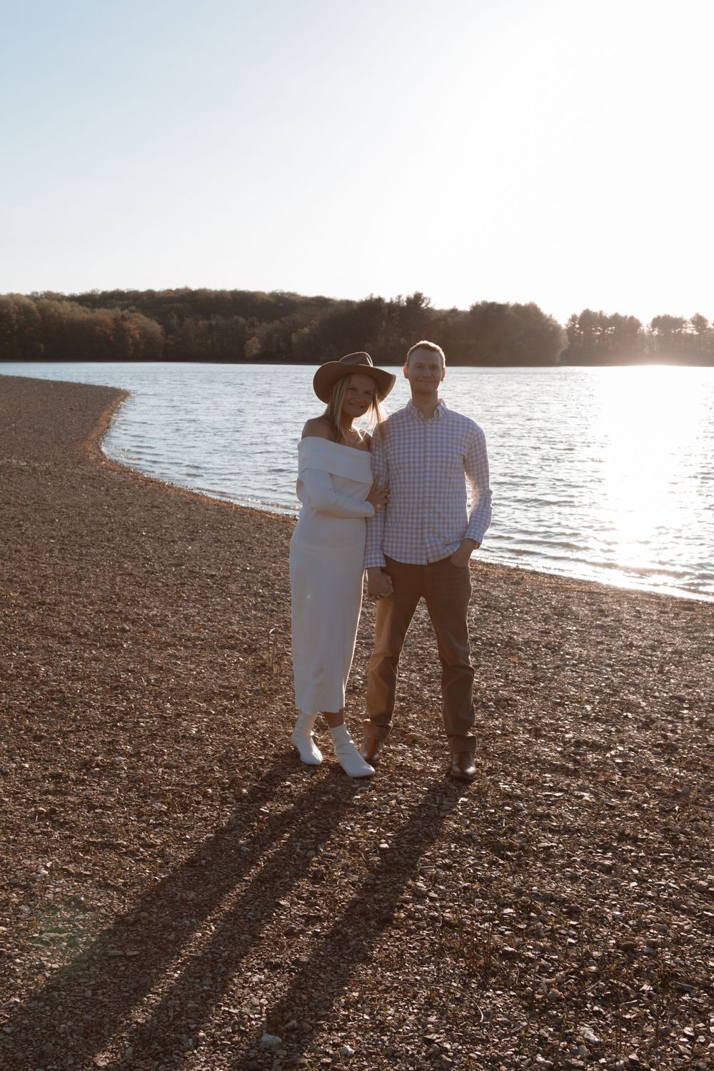 Couple stands together against sunset backdrop on rocky beach.