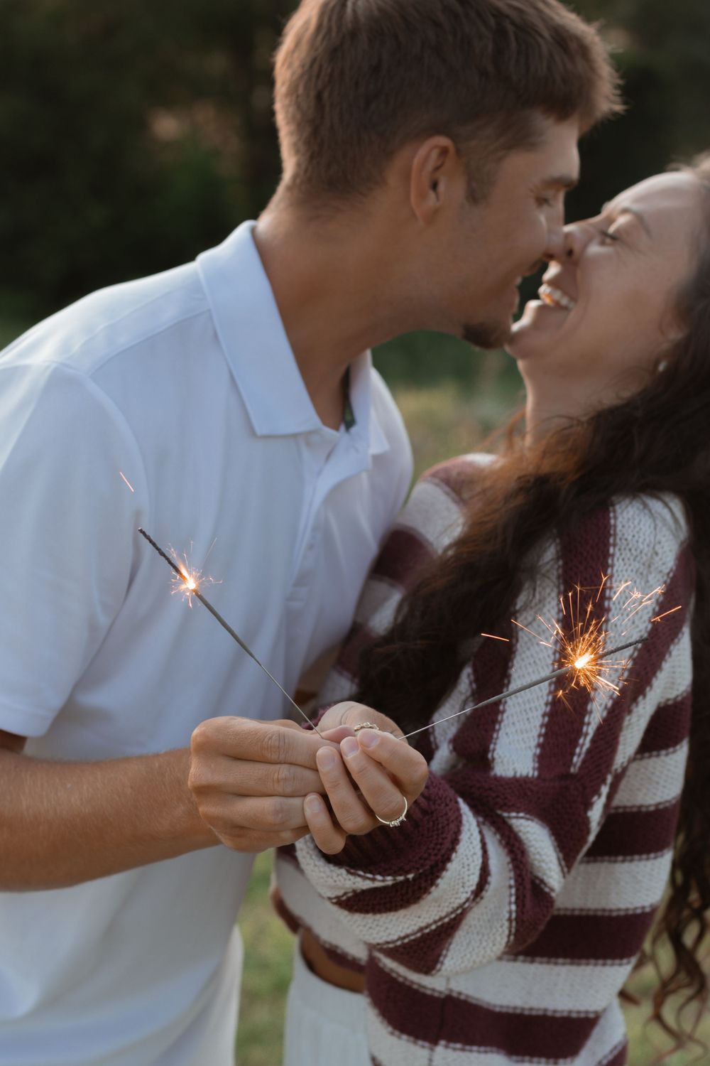 Happy couple shares an intimate moment while holding sparklers in an outdoor setting at dusk.