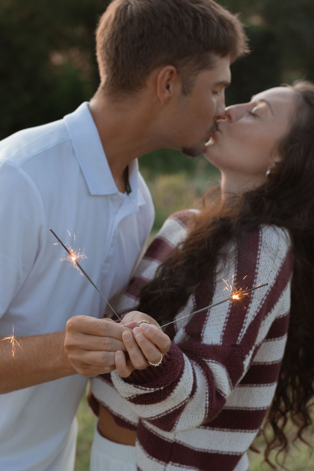 A couple in white and burgundy sweater sharing a sparkler in a romantic outdoor photoshoot series.