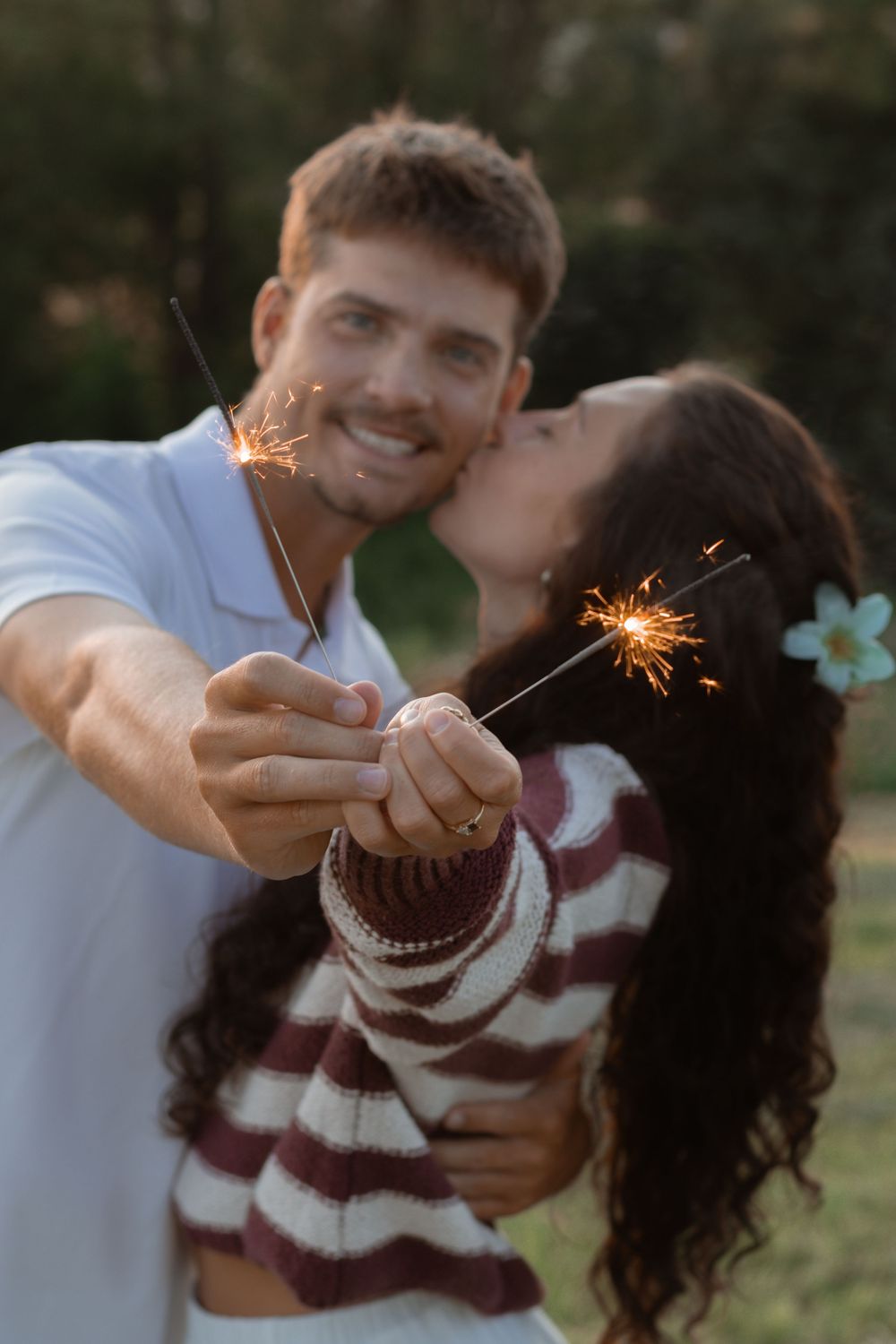 A couple holding sparklers together while embracing outdoors during a romantic moment.