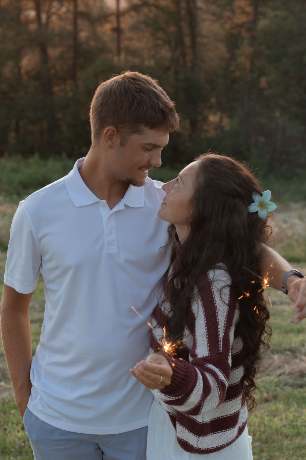 A romantic couple sharing a tender moment outdoors at sunset while holding sparklers in their hands.