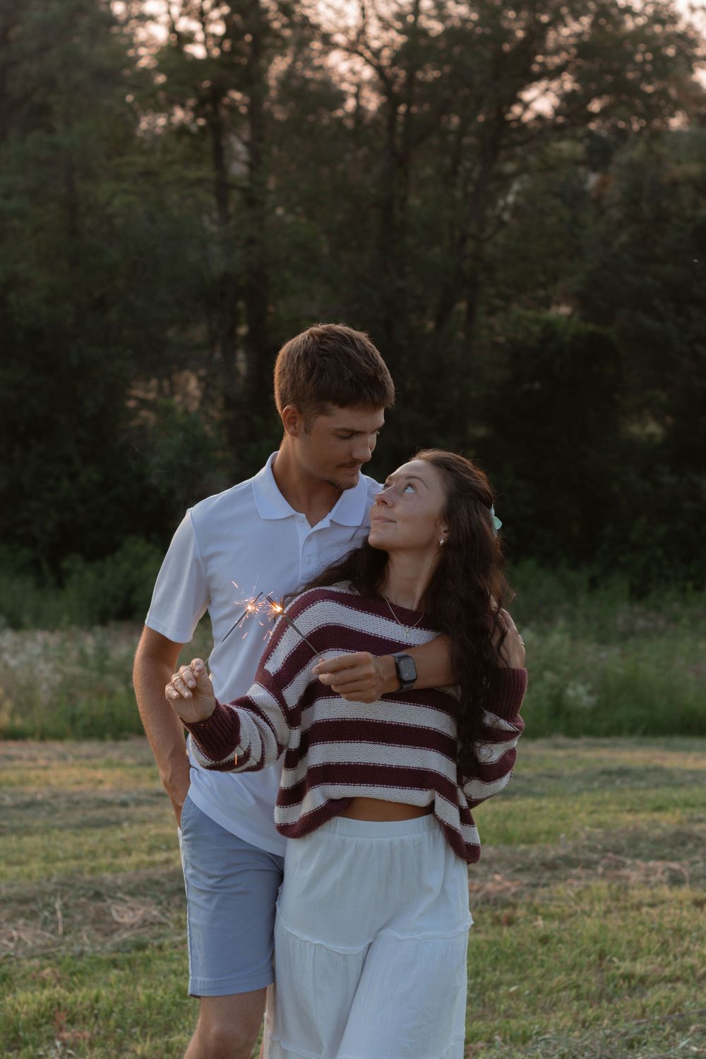 A couple embraces in a romantic field at sunset while wearing coordinated white and striped outfits.