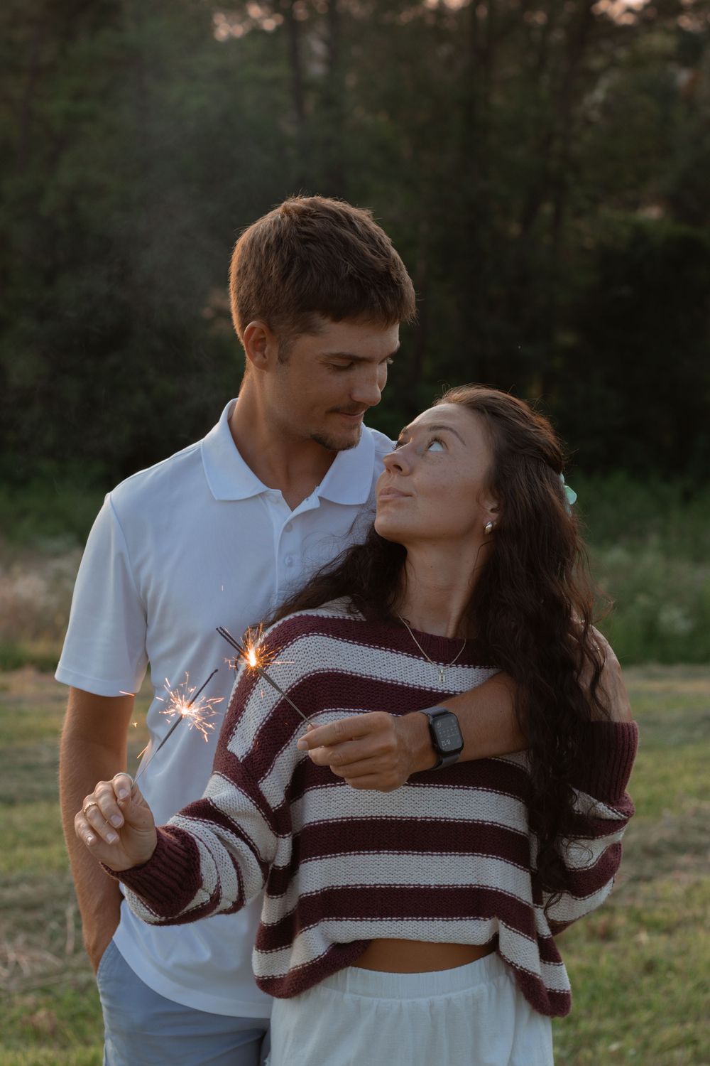 A romantic couple holding sparklers share an intimate moment at sunset in a field.