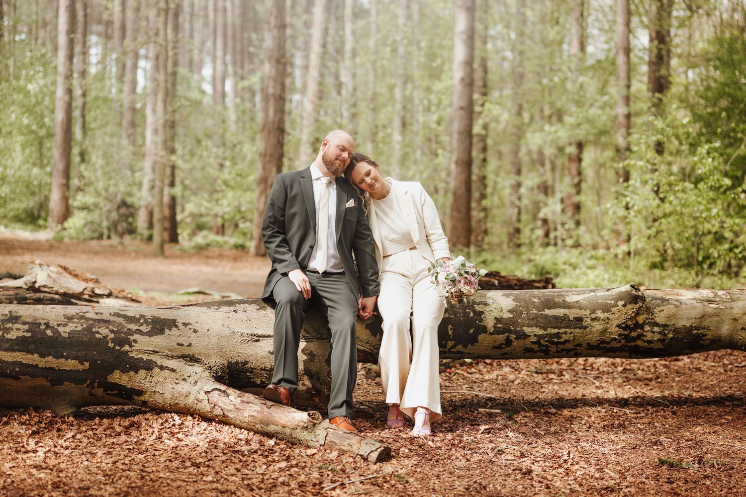 A couple sits together on a fallen log in a serene forest setting.