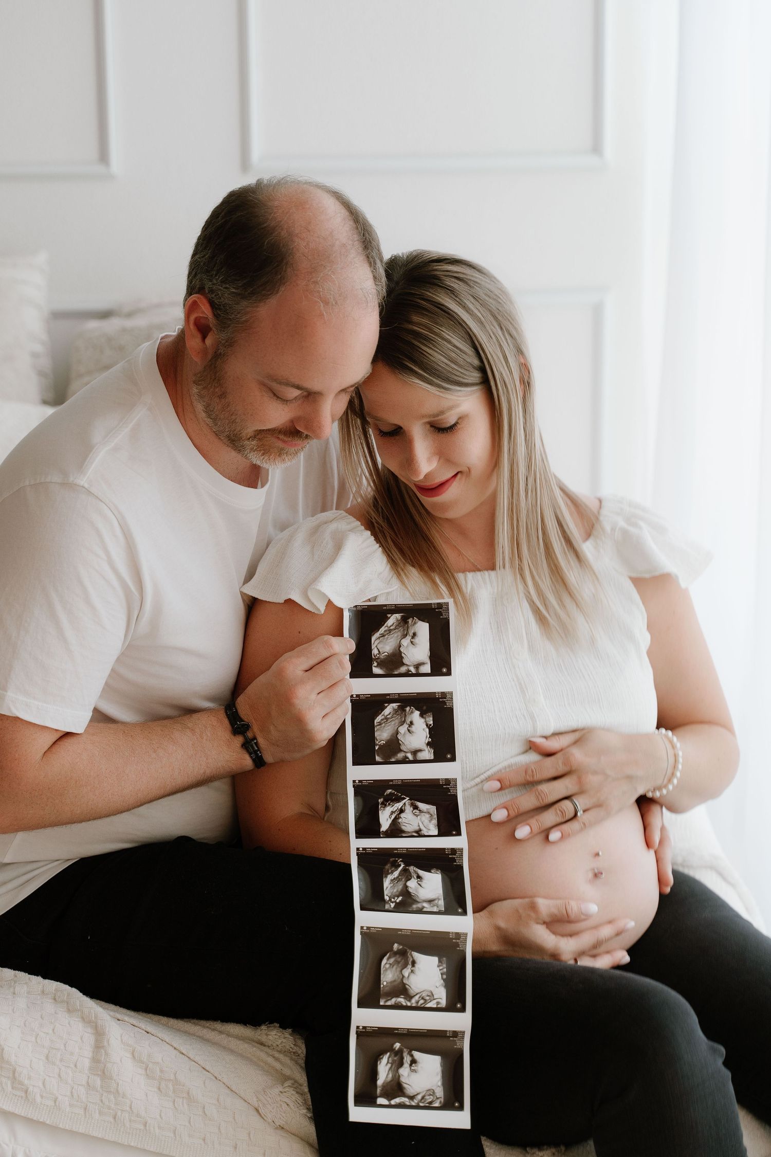 Pregnant woman sitting on floor holding bouquet of pink tulips with bare baby bump showing.