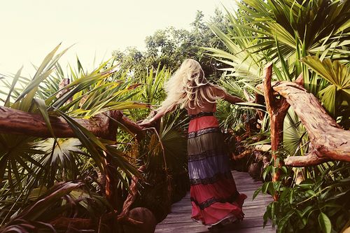 Tropical garden pathway with palm fronds and wooden walkway in warm sunset lighting.
