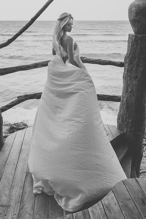 Artistic black and white bridal portrait on oceanfront deck with flowing white dress.