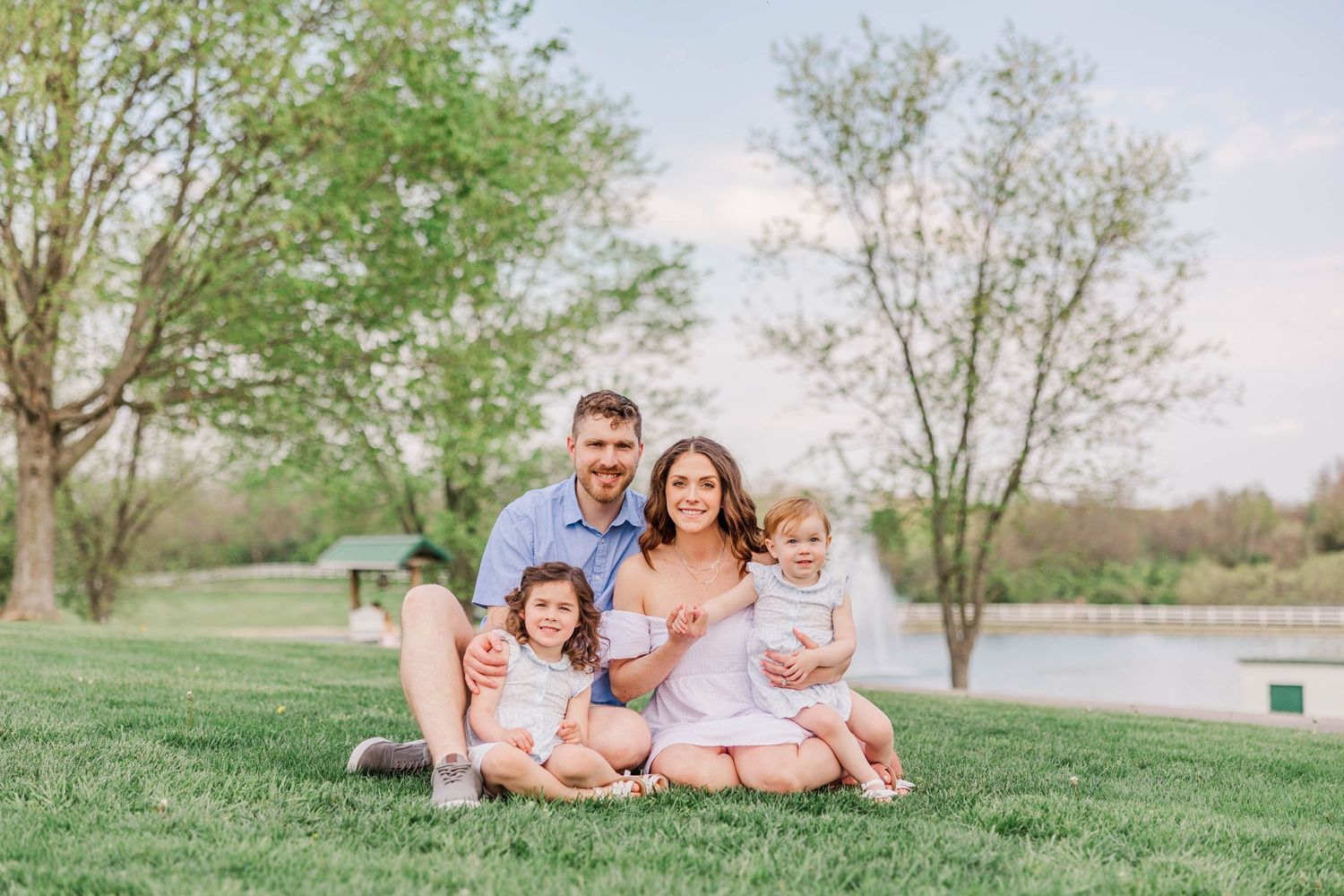 Family sitting together on grassy hill near pond during spring day.