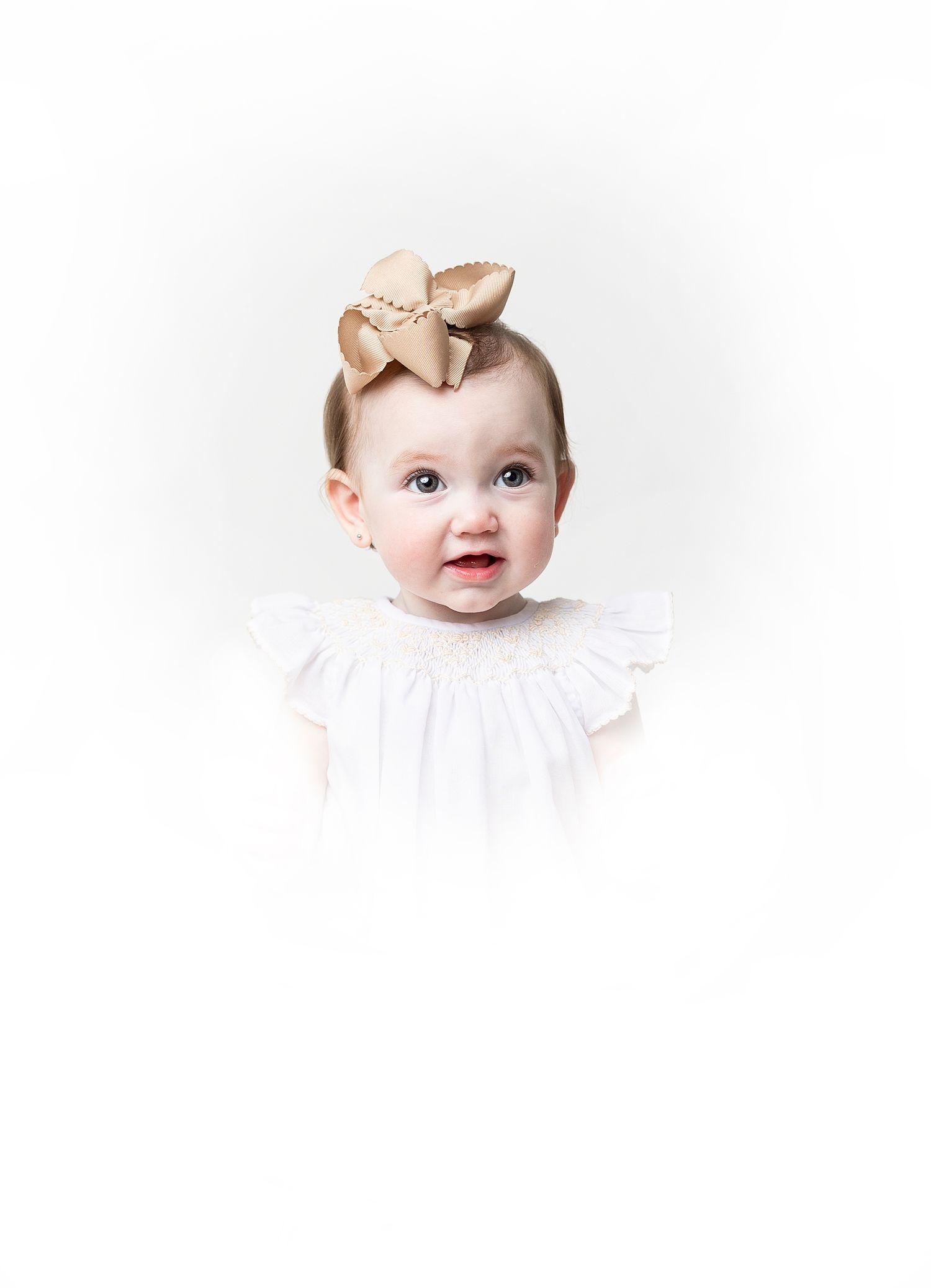 Adorable baby wearing a white dress and gold bow headband on a white background.