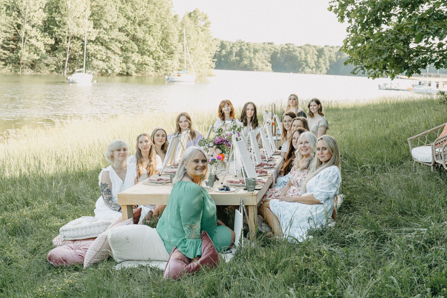 Group of women gathered at an outdoor table by a lake for a garden party celebration.