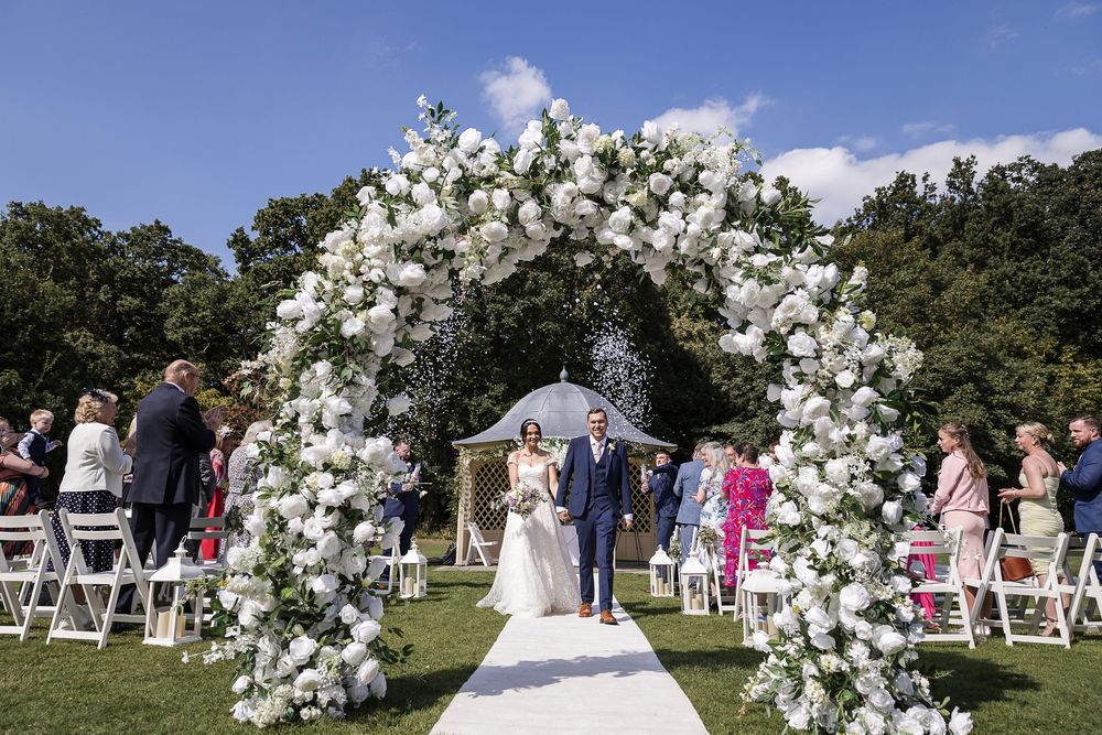 Elegant outdoor wedding ceremony setup with white floral arch at Kelham House.