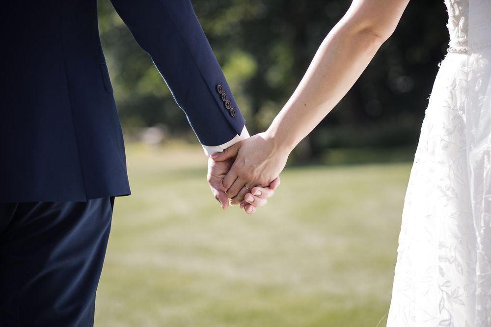 A close-up view of newlyweds holding hands outdoors during their wedding celebration at Kelham House.