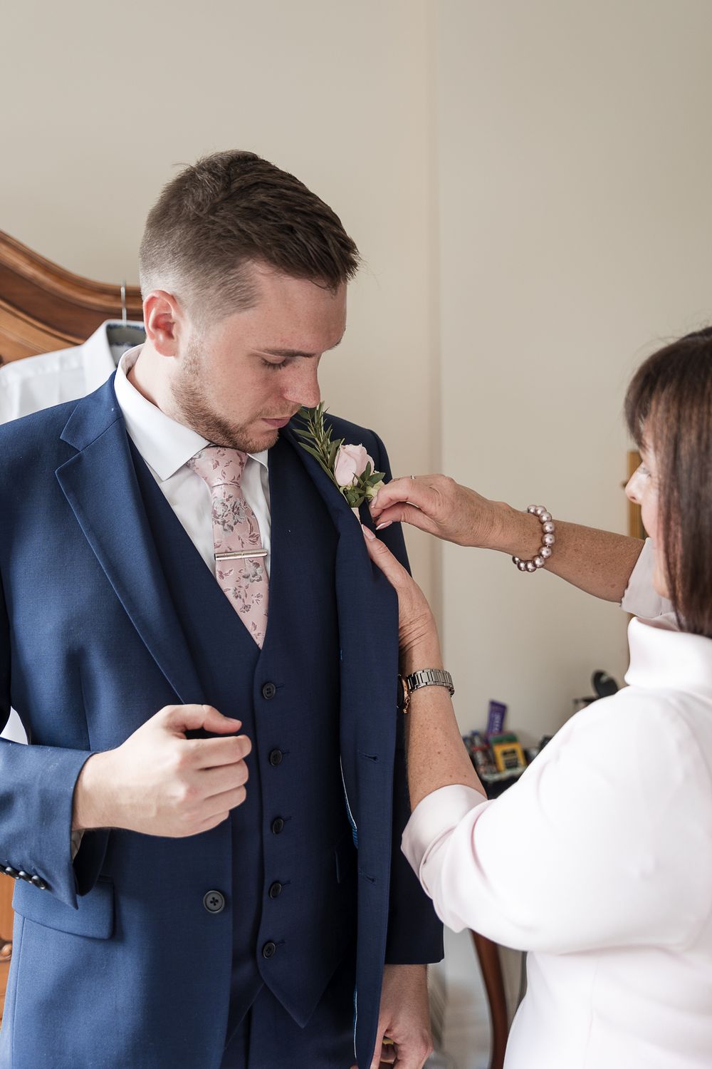 A groom in a navy suit gets his boutonniere pinned on during wedding preparations at Kelham House.