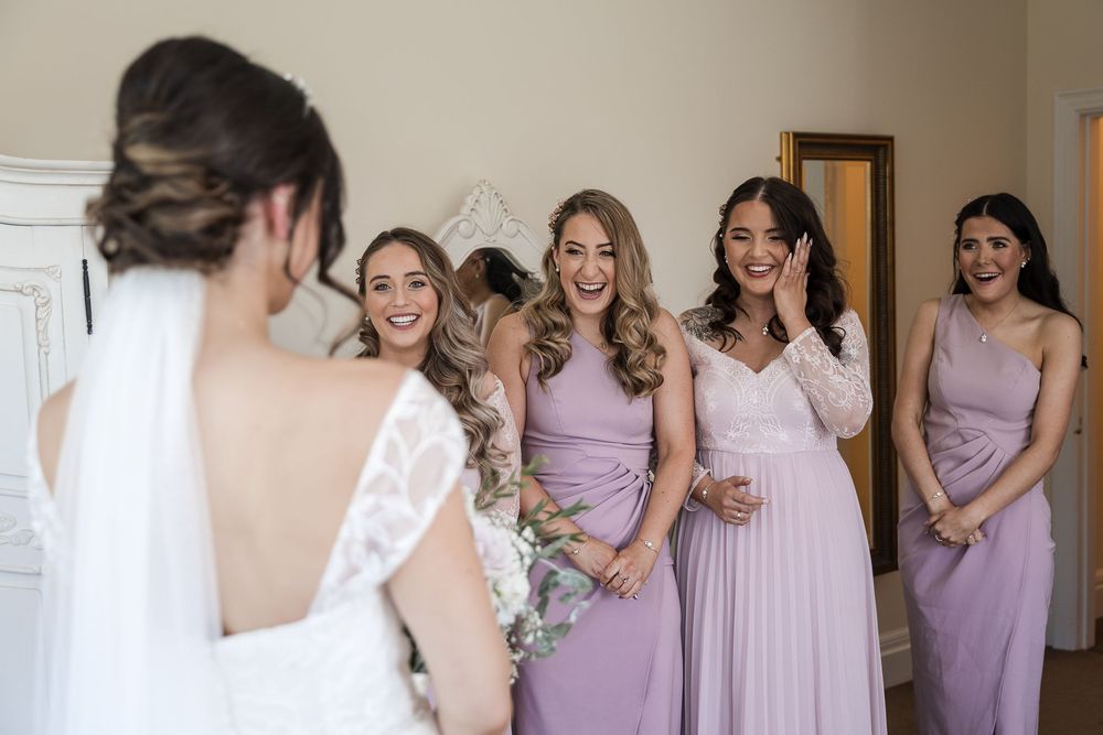 A group of bridesmaids in lavender dresses share joyful moments while getting ready for a wedding celebration at Kelham House.