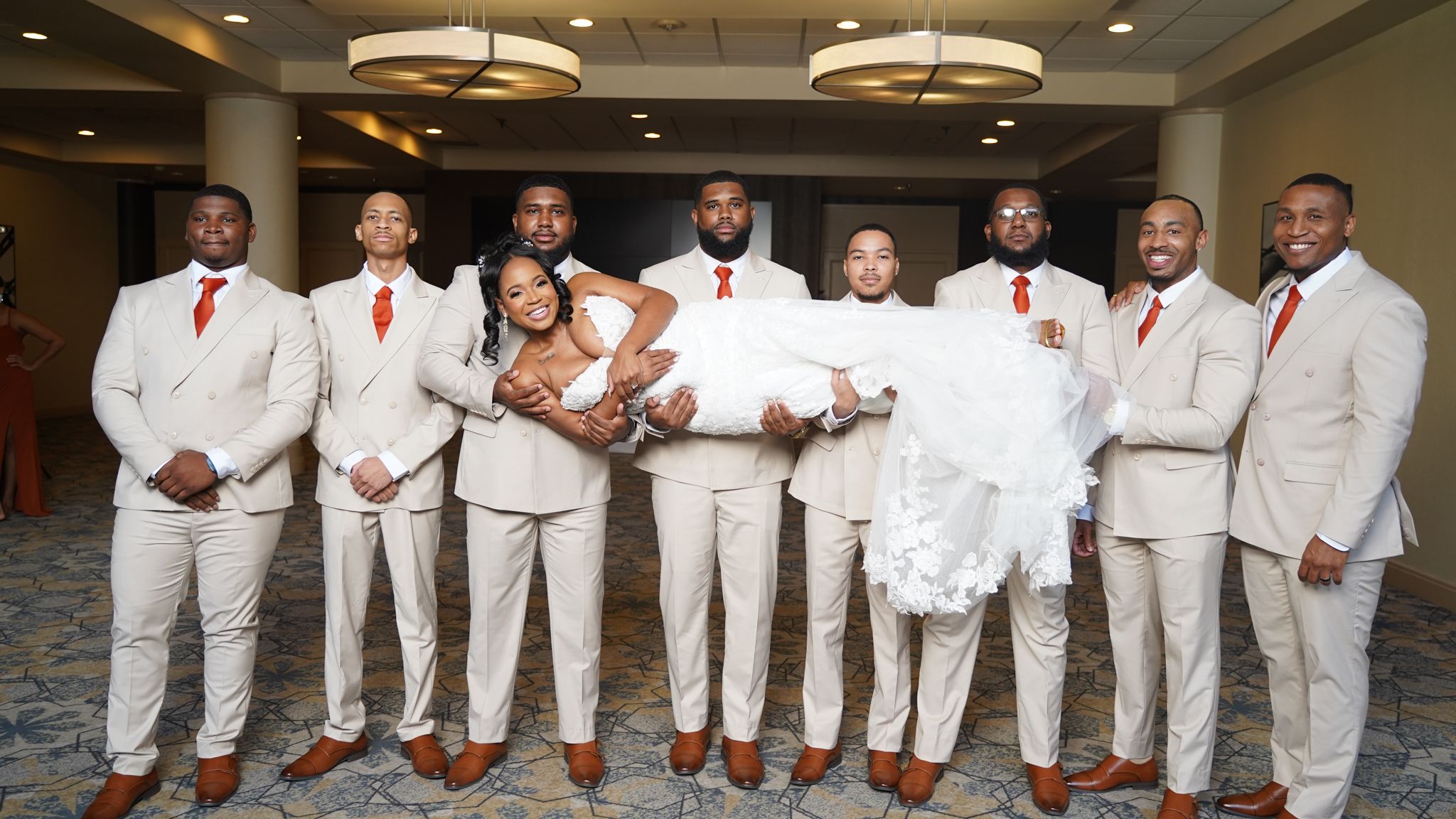 Wedding party members in white suits and red ties pose together during formal wedding photos.
