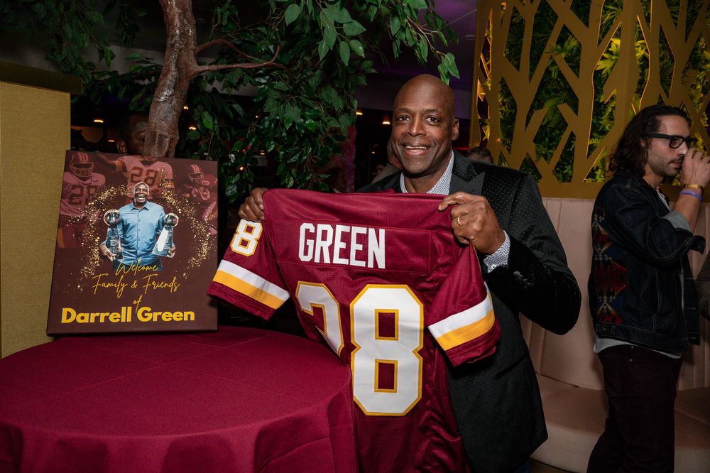 A person in a suit holds up a burgundy and gold football jersey with the number 28 and name 'GREEN' on display.