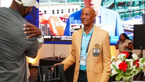 A person in a gold Pro Football Hall of Fame jacket speaks at a podium during an induction ceremony.