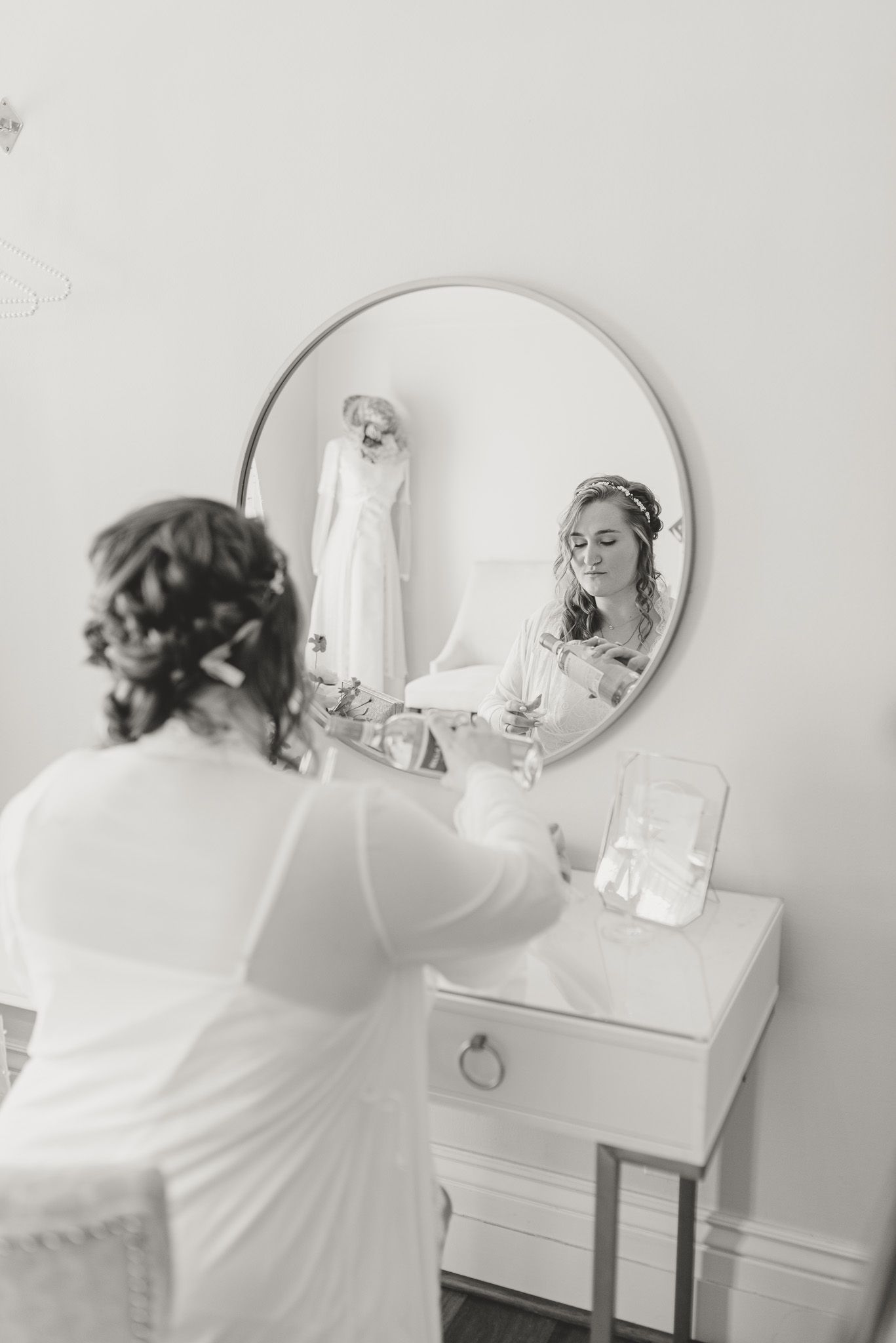 Bridal preparation scene reflected in vanity mirror with wedding dress hanging.
