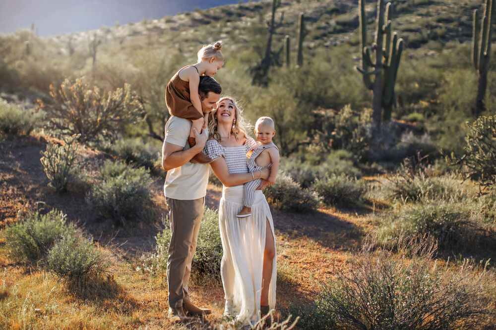 Family of four poses together on desert trail with saguaro cacti at sunset.